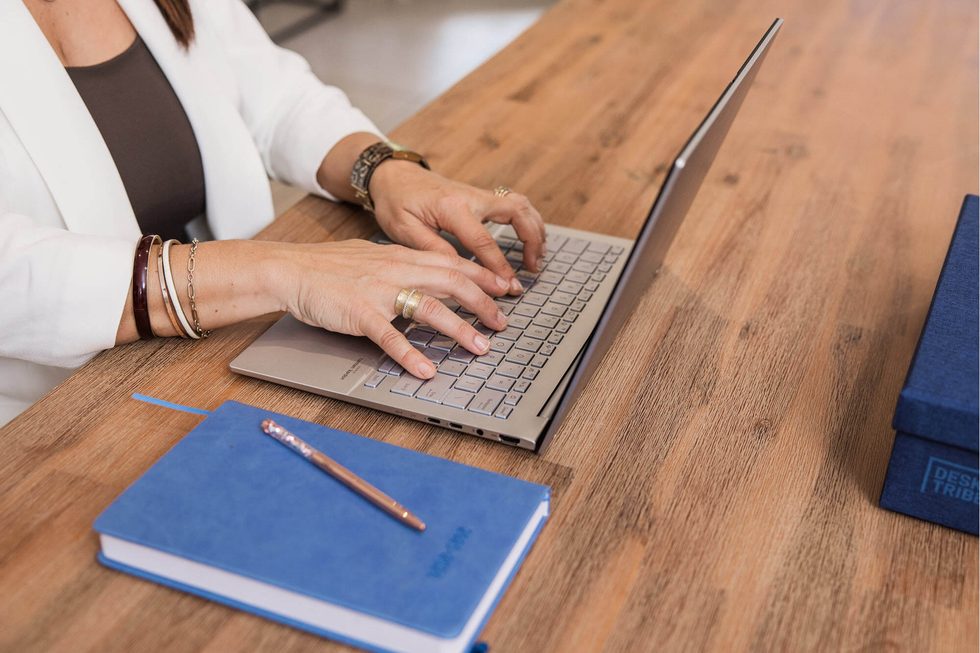 Close-up of a bookkeeper’s hands typing on a laptop at a timber desk, logging in to secure accounting software