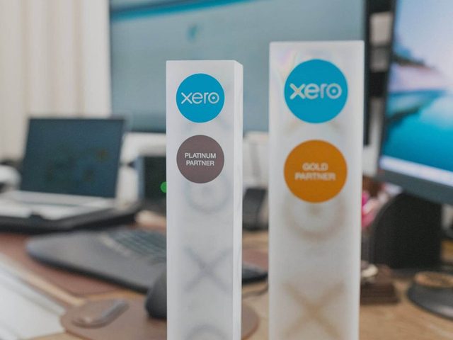 Xero partner award trophies on a desk beside two monitors