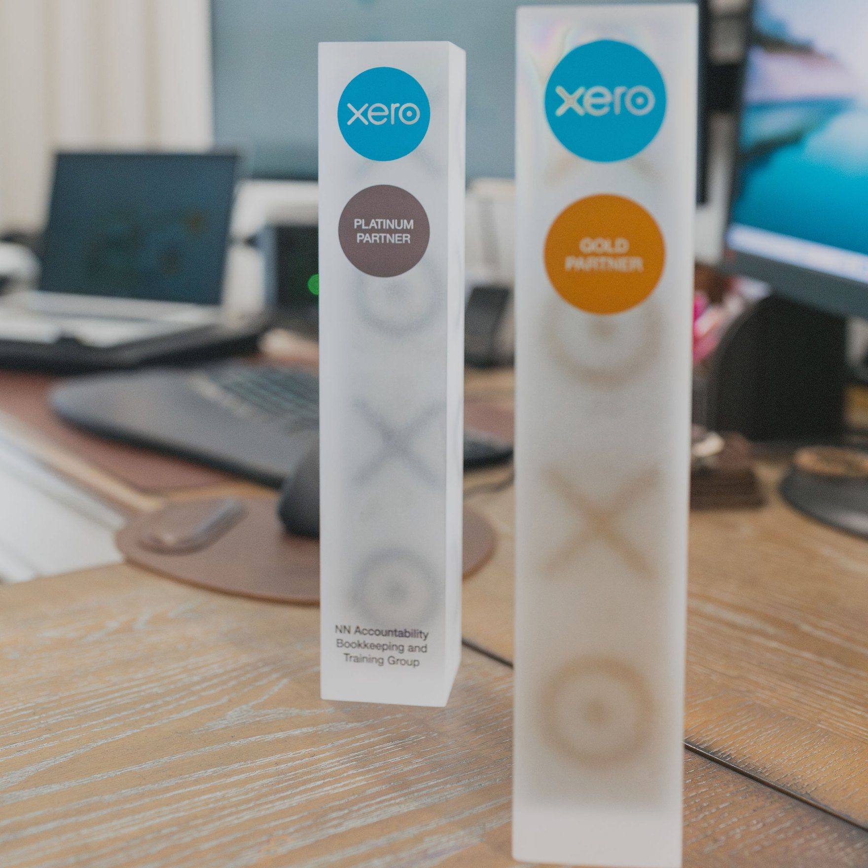 Xero Platinum and Gold Partner awards on a desk in front of the office computers